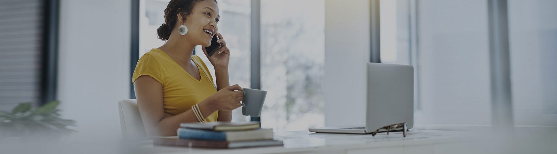 Woman on phone sitting at desk with coffee